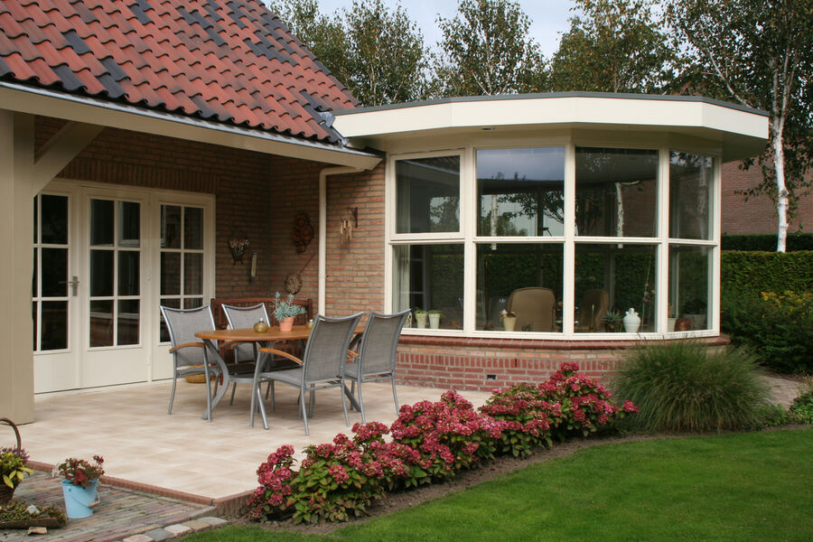 Brick house with a sunroom addition and patio seating beside a landscaped backyard